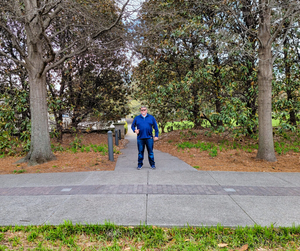 Man standing on a pathway in a park with trees and pathway as frame. This photo is an example of framing in a picture using environmental elements. One of the technique for how to make your family photos and videos look AMAZING.