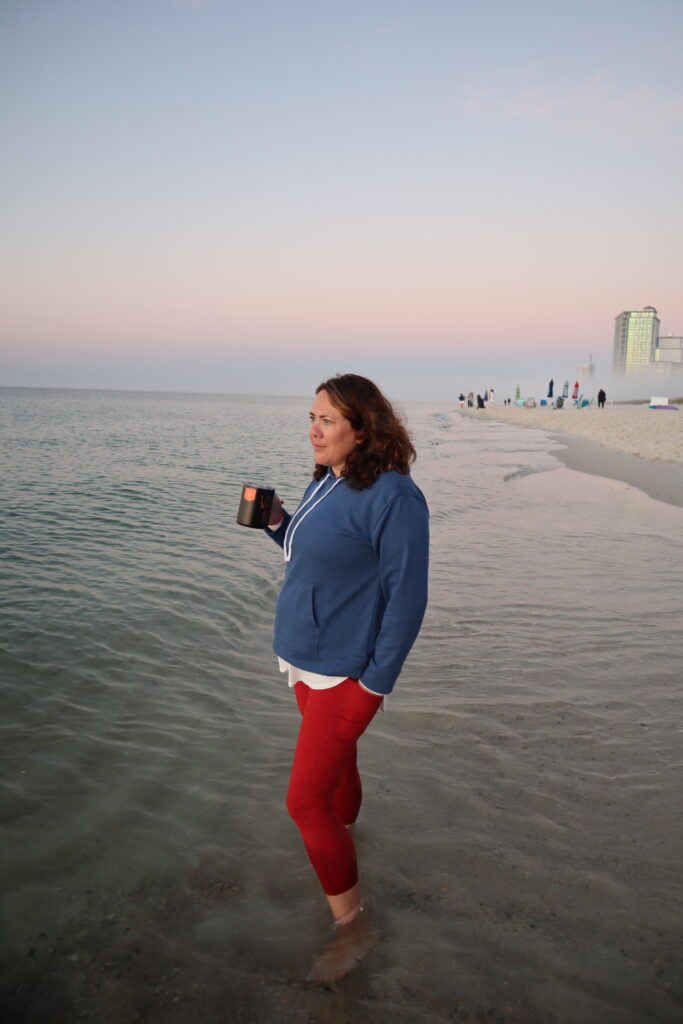 Photo of a woman standing in the ocean drinking coffee early in the morning. This an example of taking a candid photo using composition techniques. This is part of the How to make your family photos and videos look AMAZING blog post. 